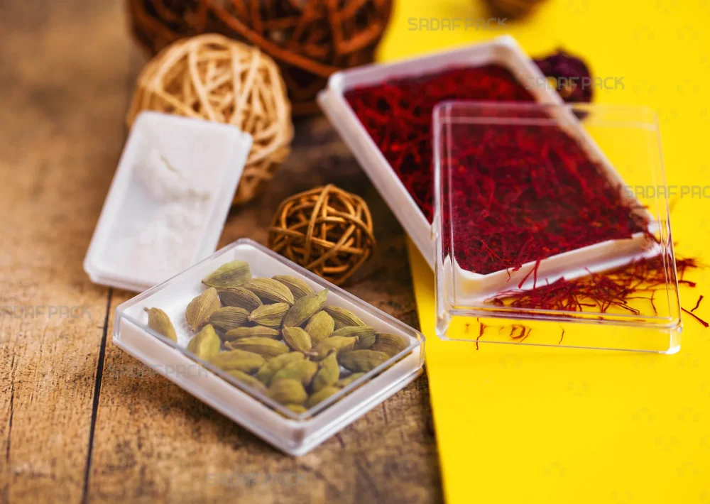 ظروف کریستالی مستطیل اسپانیا صدف پک، مناسب برای بسته‌بندی و نمایش زعفران و هل، که در تصویر یکی با زعفران سرگل، دیگری با هل سبز پر شده است.