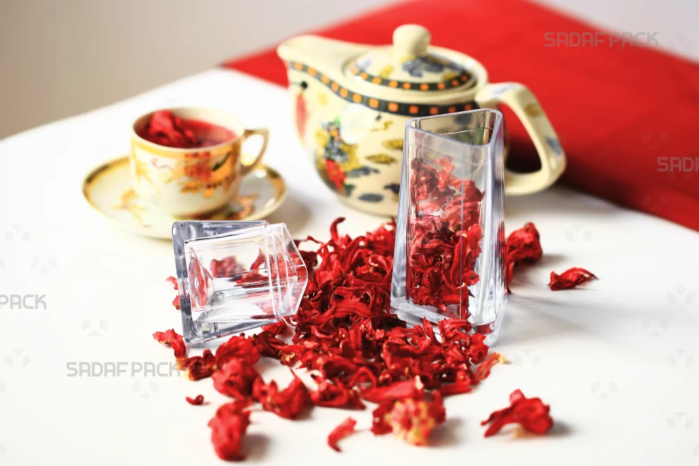 مایی از ظرف باز شده سری الماس صدف پک به همراه درب آن، پر شده با گلبرگ‌های خشک مناسب دمنوش
