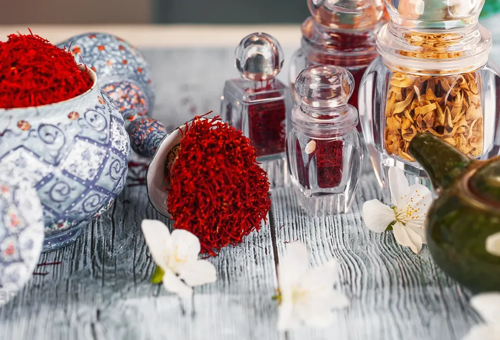 مجموعه‌ای از ظروف کریستالی لوکس صدف پک سری گوهر کف بالا که با زعفران صادراتی سرگل و ریشه پر شده‌اند و در یک چیدمان زیبا برای نمایش بسته‌بندی شیک و مناسب هدیه قرار گرفته‌اند.
